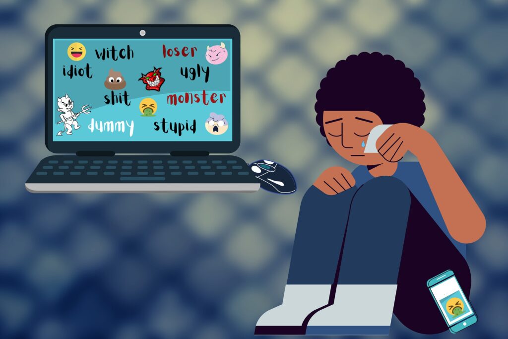 Ragazzo seduto e piangente davanti ad un computer su cui si vedono parole di disprezzo e sul pavimento a fianco un cellulare su cui si vede uno smile d'odio