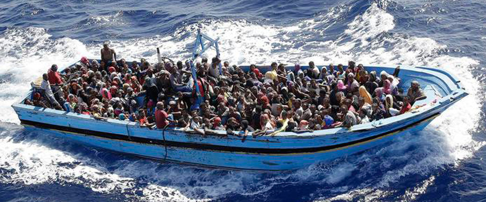 Primo piano di un barcone strapieno di migranti nel mare mosso 