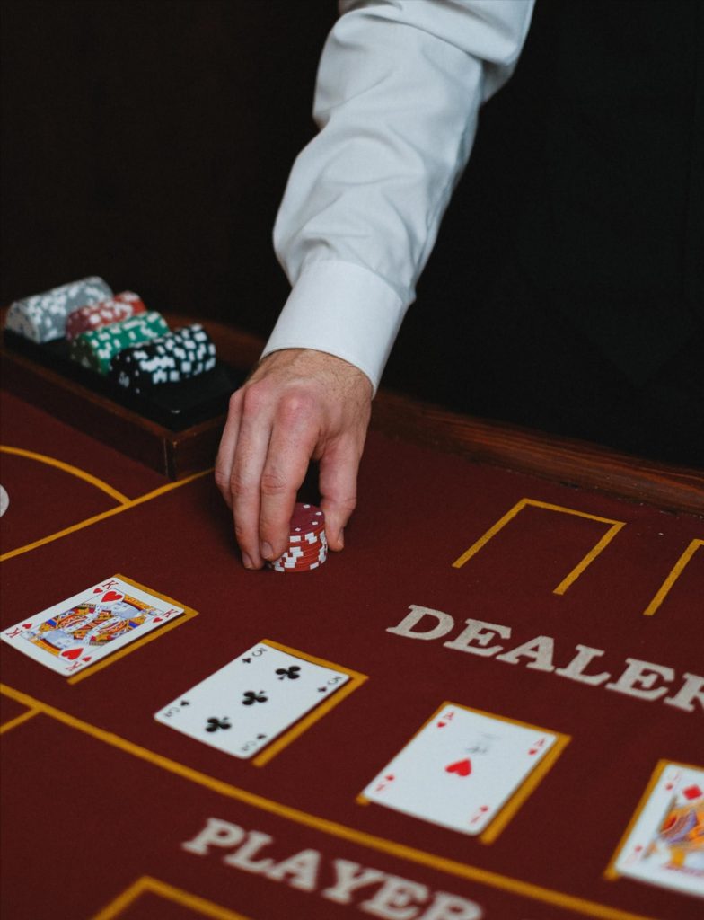 Immagine di un tavolo da gioco dove sono disposte delle carte e dove si vede una mano in primo piano che sta posando una pila di fiches