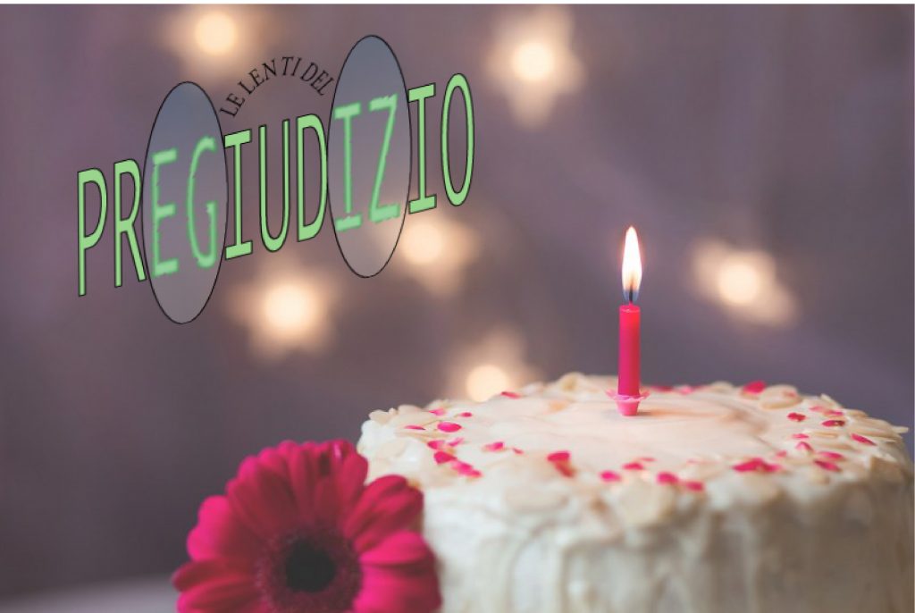 in primo piano una torta con una candelina accesa nel centro e al lato della torta un fiore, sullo sfondo delle luci sfocate con il logo delle lenti del pregiudizio.